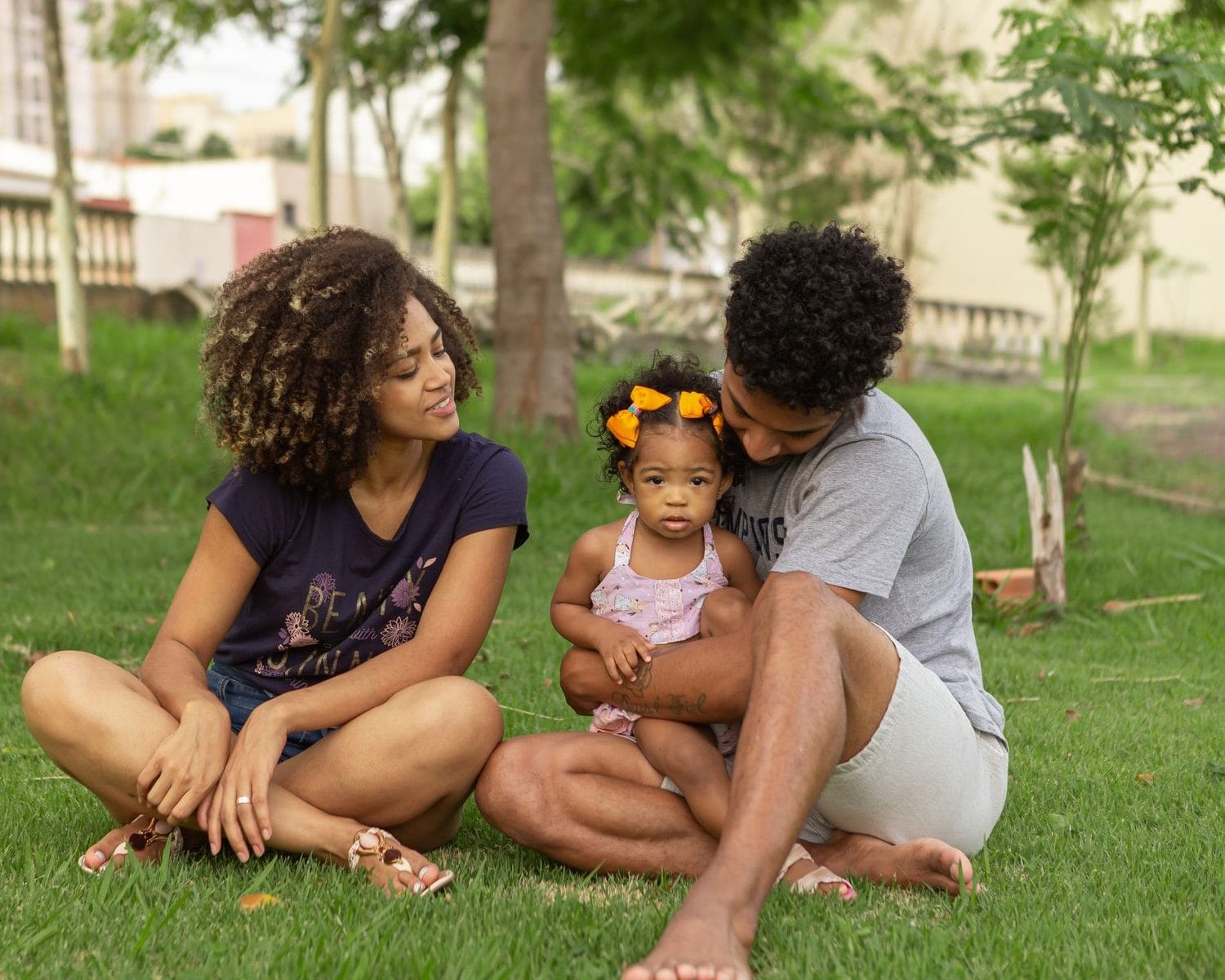 Pai, mãe e a filha bebê sentados na grama de uma praça