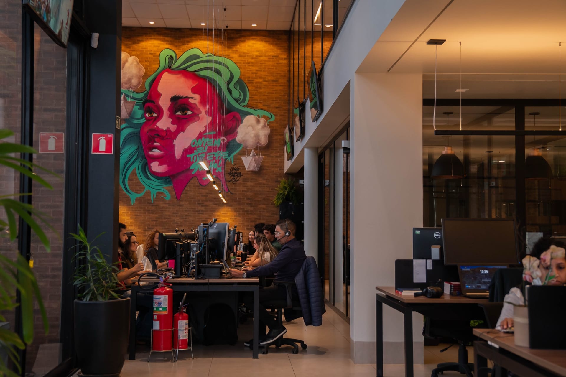 Salão da matriz da Finanto com grafite na parede de tijolos e o time trabalhando